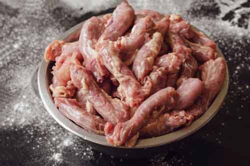 Raw chicken necks in a metal bowl on a black with white backgrou