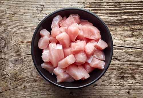 Raw cut meat chunks in black bowl on wooden table, top view
